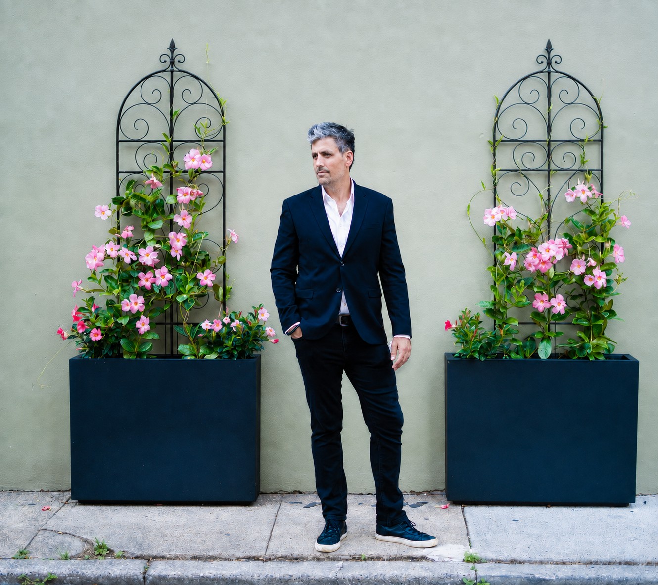 Brody Bond standing between two planters of pink mandevilla against a pale wall