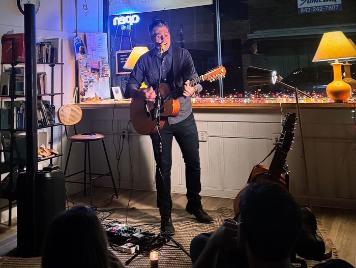 Playing a twelve-string at the counter, listeners a few feet away