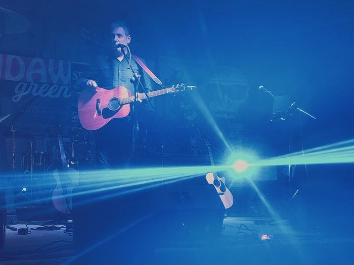 A stage washed in blue light, guitar in hand