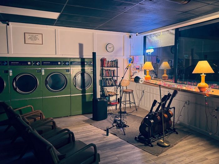 A laundromat set for a show before doors: a microphone, guitars on a rack, lamps and armchairs