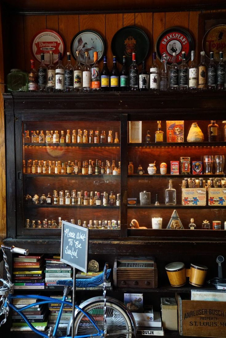 A lit cabinet of miniature bottles above shelves of cocktail books at NEATFREAK!